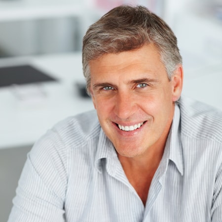 Older man wearing a grey shirt and smiling thanks to an inlay