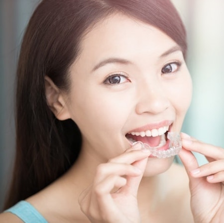 Woman smiling while holding Invisalign aligner, showcasing clear dental treatment option for misaligned teeth at Dental Group of Westchester.