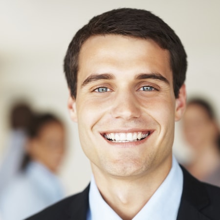 Smiling man in a suit showcasing a healthy, restored smile, reflecting the benefits of restorative dental treatments like crowns and bridges.