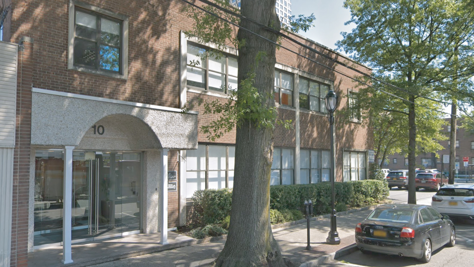 Dental Group of Westchester building entrance at 10, featuring glass doors, brick facade, and surrounding greenery, located in White Plains, NY, serving diverse community dental needs.
