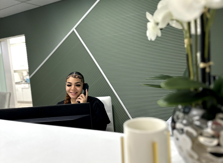 Receptionist at Dental Group of Westchester answering phone call in a modern office setting, with green accent wall and decorative plant.