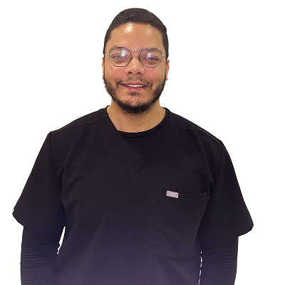 Julio Rosario, dental assistant at the Dental Group of Westchester, wearing a black scrubs top and glasses, smiling warmly against a plain white background.