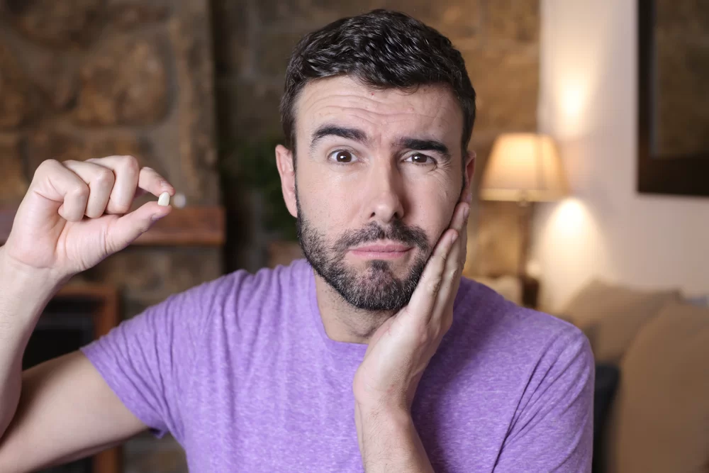 Man in a purple shirt holding a tooth and showing signs of pain, representing a dental emergency related to a knocked-out tooth.