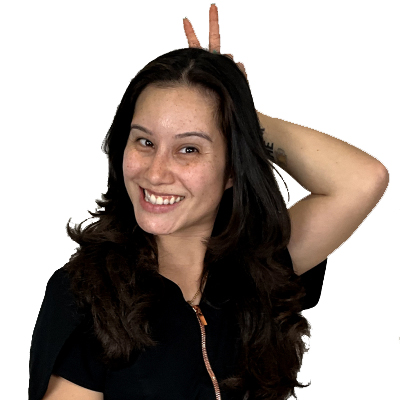 Head dental assistant Michelle Estrada smiling and playfully holding up a peace sign behind her head, showcasing a friendly and approachable demeanor in a professional dental setting.