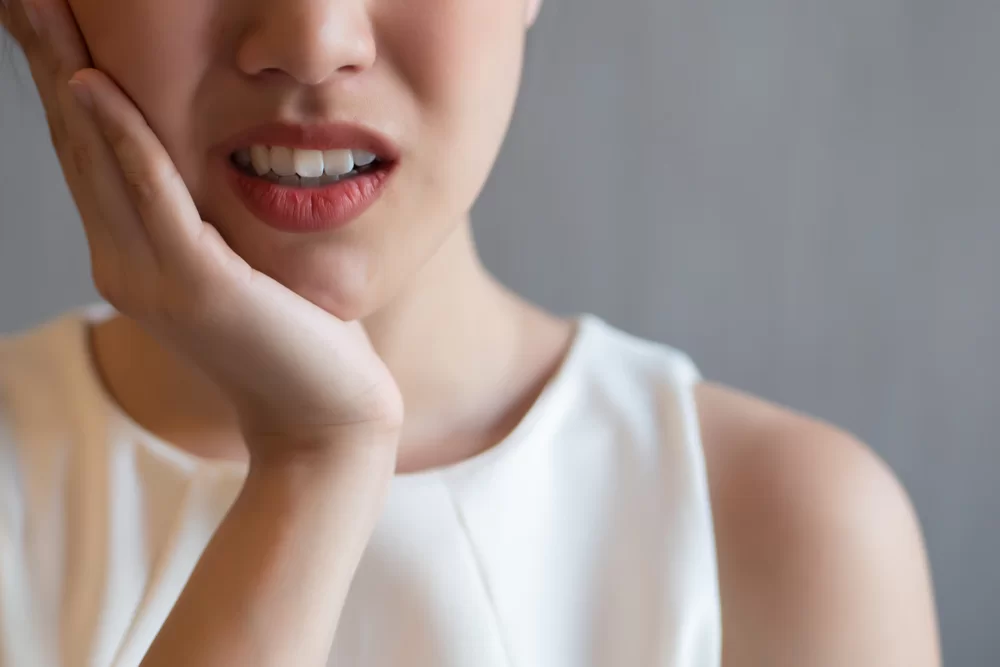 Woman experiencing dental pain, holding her jaw, showing discomfort, relevant to emergency dental care services for cracked or broken teeth.