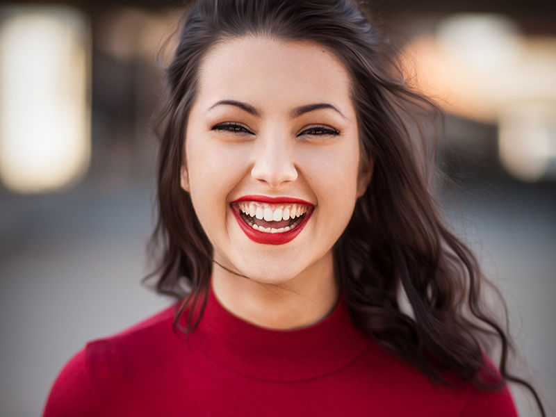 Smiling woman in a red top, showcasing healthy teeth, reflecting positive dental experiences and care at Dental Group of Westchester.