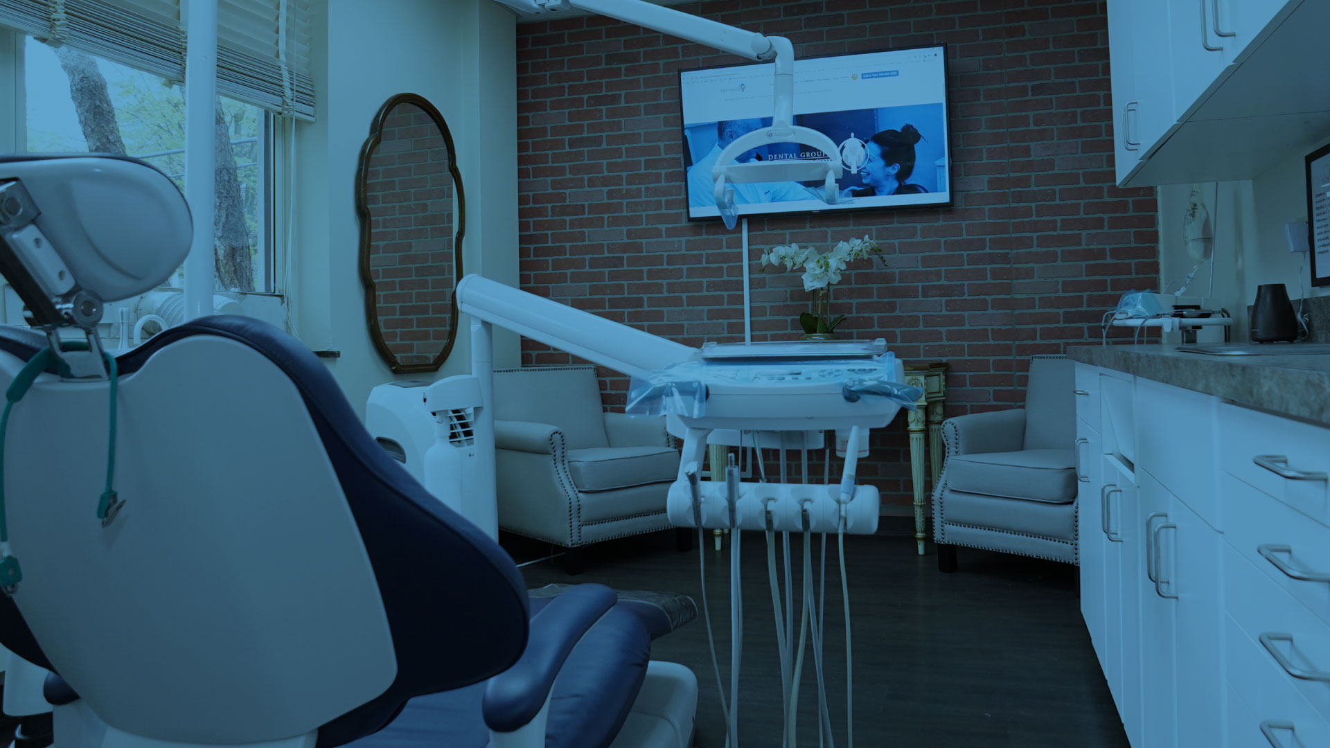 Dental treatment room featuring a dental chair, modern equipment, and a large screen displaying the Dental Group of Westchester website, emphasizing advanced periodontal care and patient comfort.