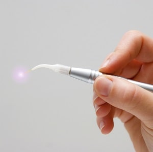 A dentists hand holds a activated dental laser system in his hand. Grey background