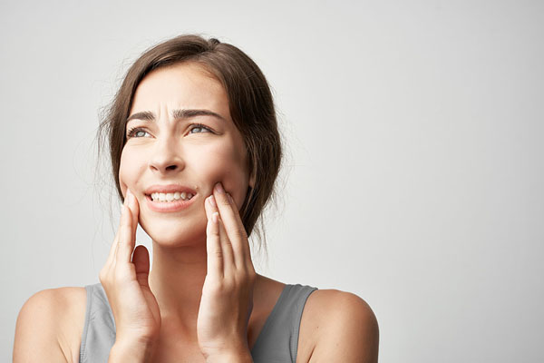 Young woman expressing pain while holding her face, indicating dental discomfort, relevant to emergency dental care services for urgent issues like dental abscesses or lost crowns.