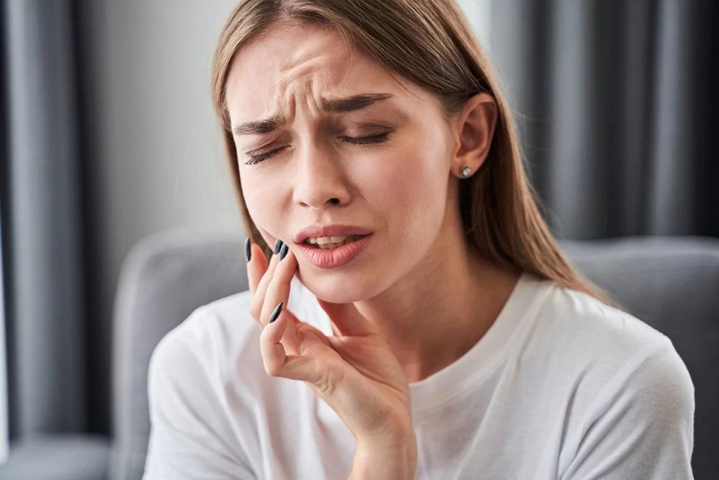 Woman experiencing severe tooth pain, holding her jaw in discomfort, highlighting the urgency of dental care for emergencies.