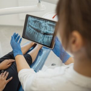 Dental professional showing dental X-ray on tablet to patient, discussing post-operative care after wisdom teeth removal.